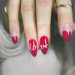 Vibrant red nails with 'love' art on a woman's hand, showcasing elegant style and design.